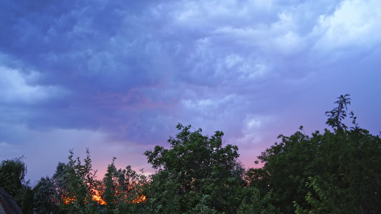 Sparkles of lightning on the cloudy sky. Strong wind moves the trees under the dark blue sky at sunset in summer. Lightning before the rain outdoors.