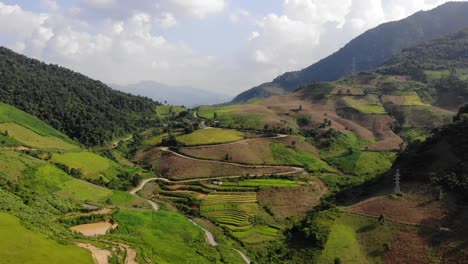 wide slow moving aerial shot of beautiful green valley with terraced fields and winding road