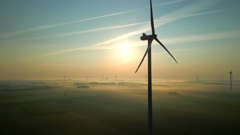 The-drone's-camera-flies-in-a-circle-around-the-spinning-propellers-of-a-wind-turbine-over-a-magical-landscape-immersed-in-fog