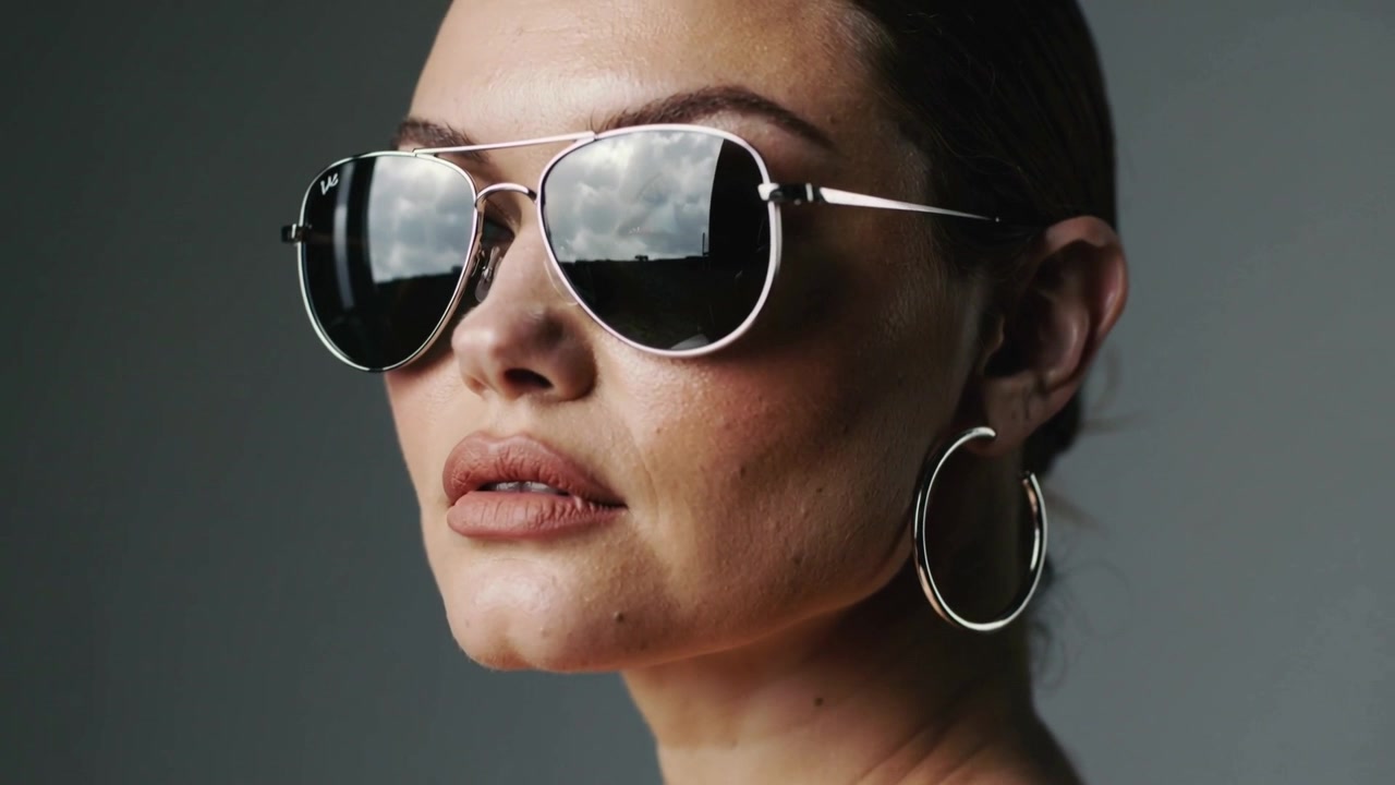 Posing model tilting face while lens panning in studio, mirror aviators, hoop earring during shoot