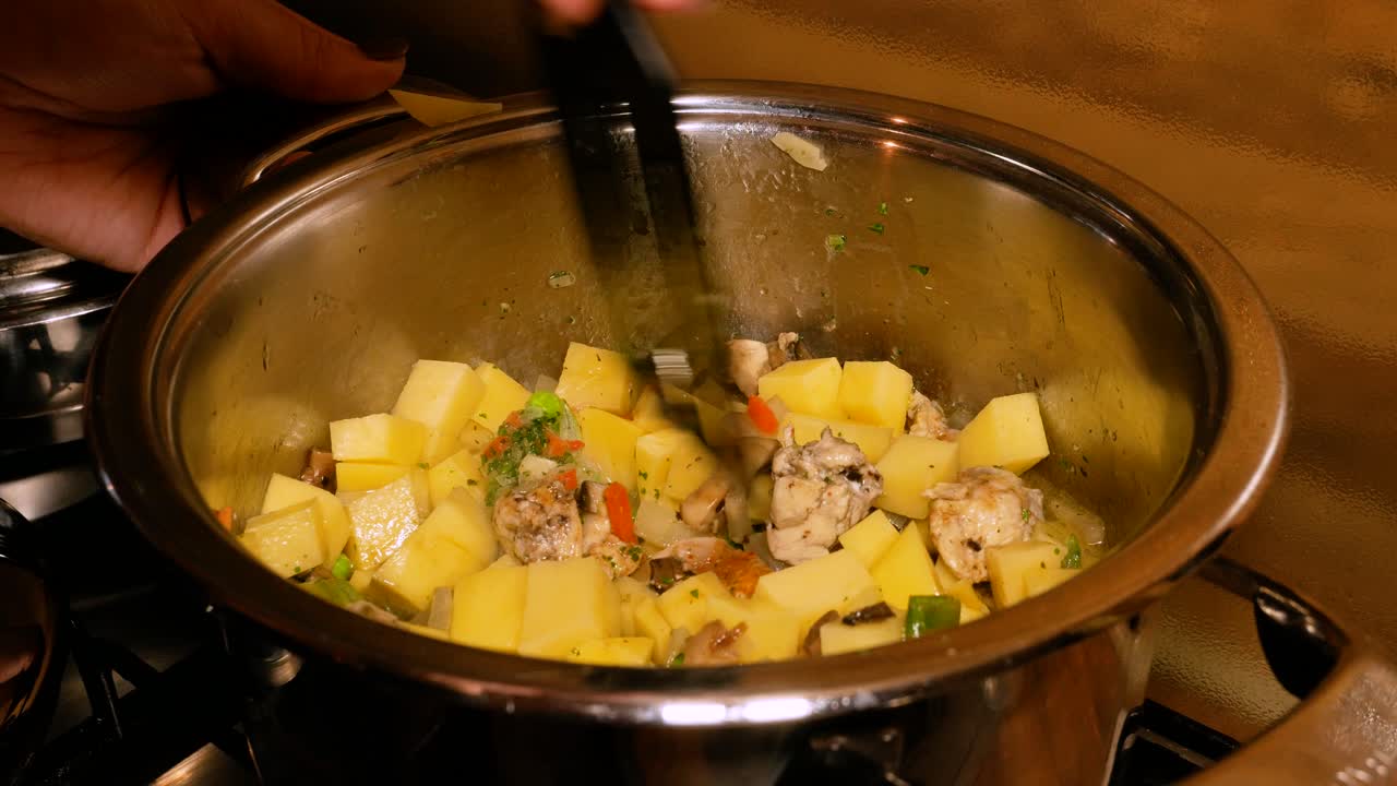 las manos femeninas están mezclando guiso humeante en una olla de acero en el horno