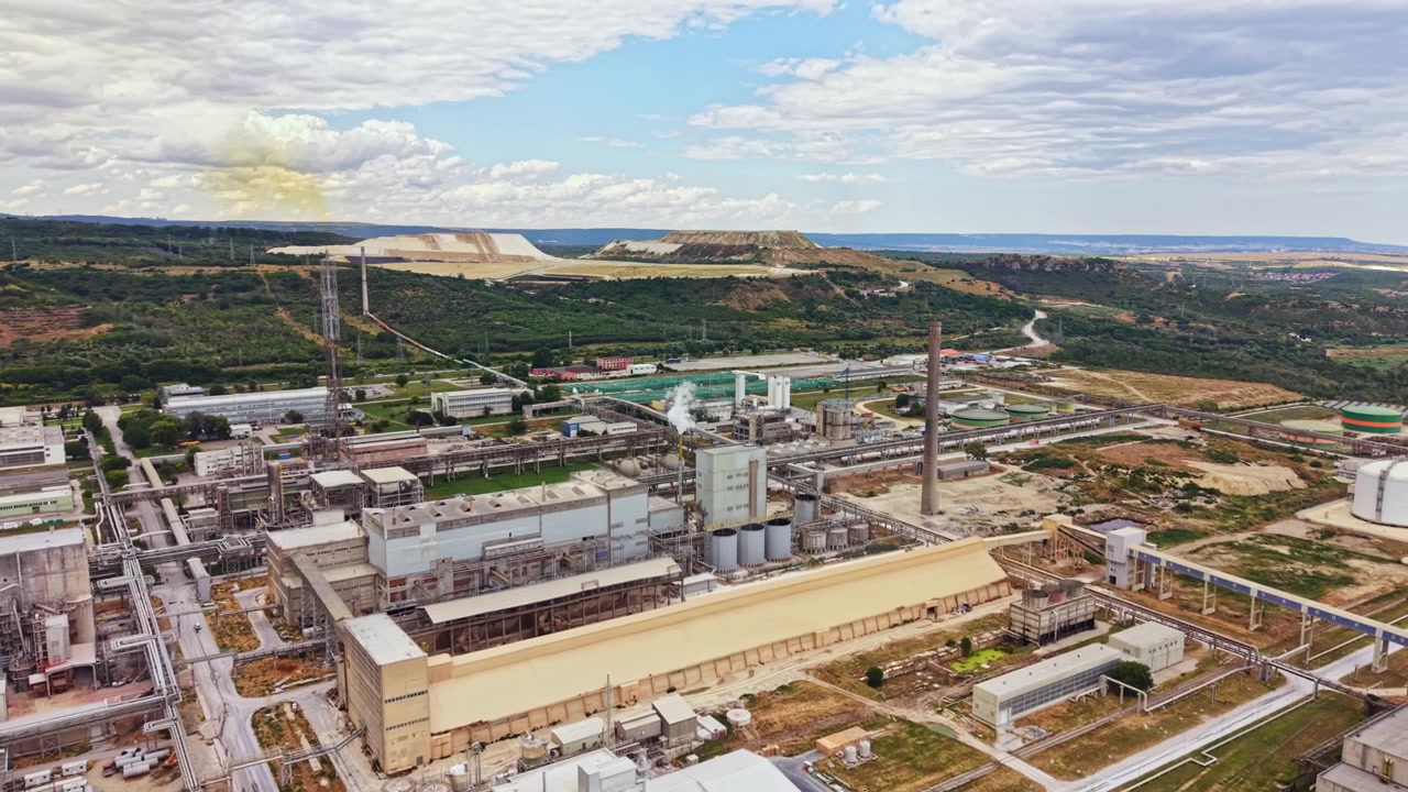 Operaciones de fábrica se desarrollan en una gran zona industrial con maquinaria y estructuras bajo un cielo azul despejado durante la tarde.