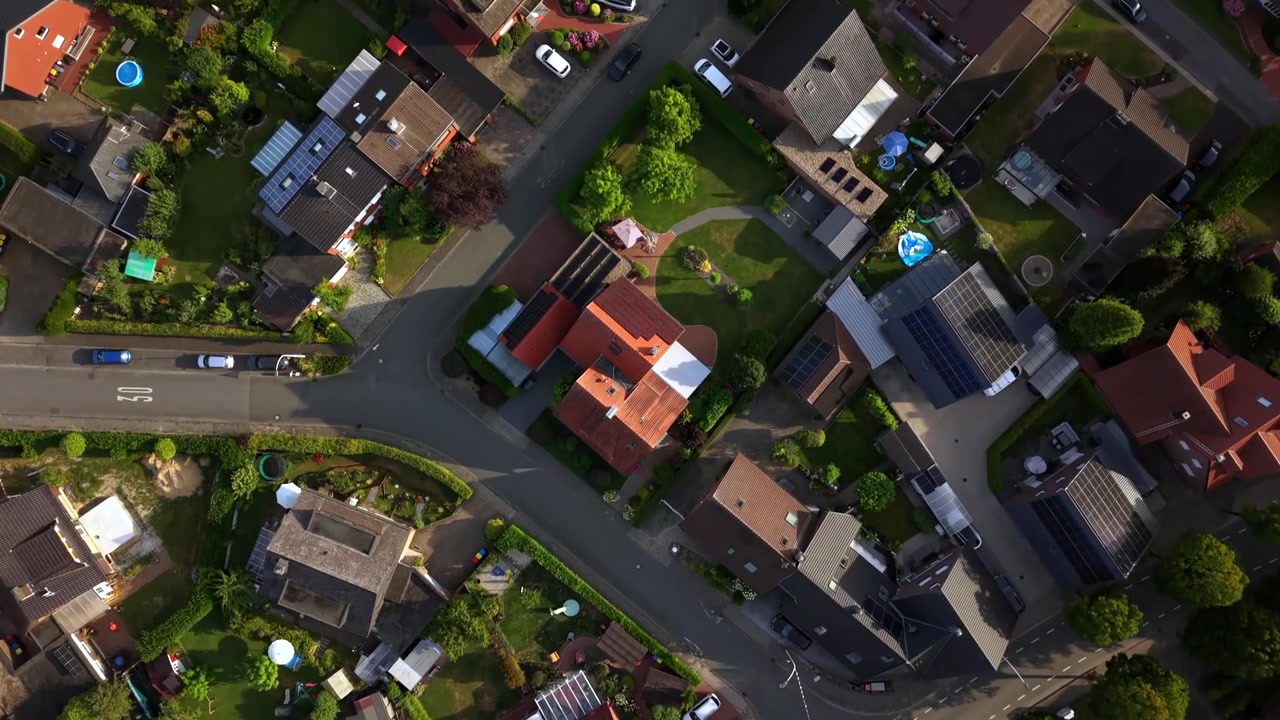 Tetti in tegole rosse circondano un tranquillo incrocio stradale in un piccolo quartiere tedesco al tramonto, giardini privati e siepi curate separano le case sotto la calda luce della sera. Ripresa aerea con drone dall'alto.