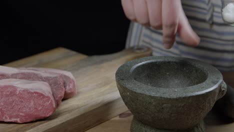 manos depositando sal en el mortero y luego lo aplasta para salpicar en el corte de carne