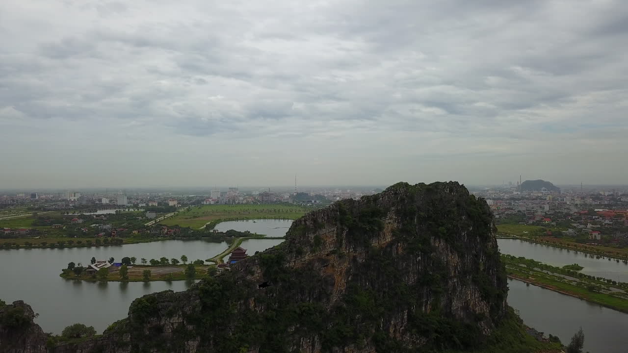 Experience a tilt-up view in the Dinh Thanh Cao Son region of Trang An, Ninh Binh, Vietnam, starting from the serene waters and rising to reveal the impressive karst rock formations under a cloudy sky