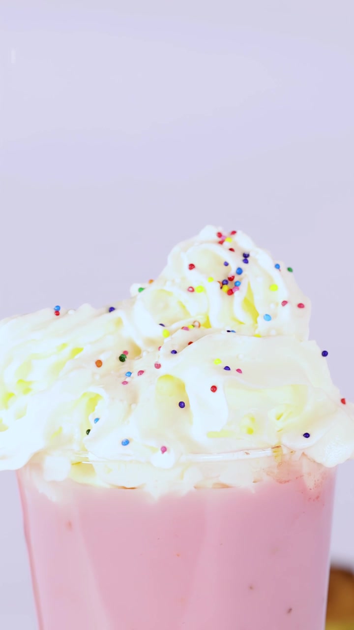 Primo piano al rallentatore di codette colorate che cadono su un milkshake rosa con panna montata, illuminazione brillante.