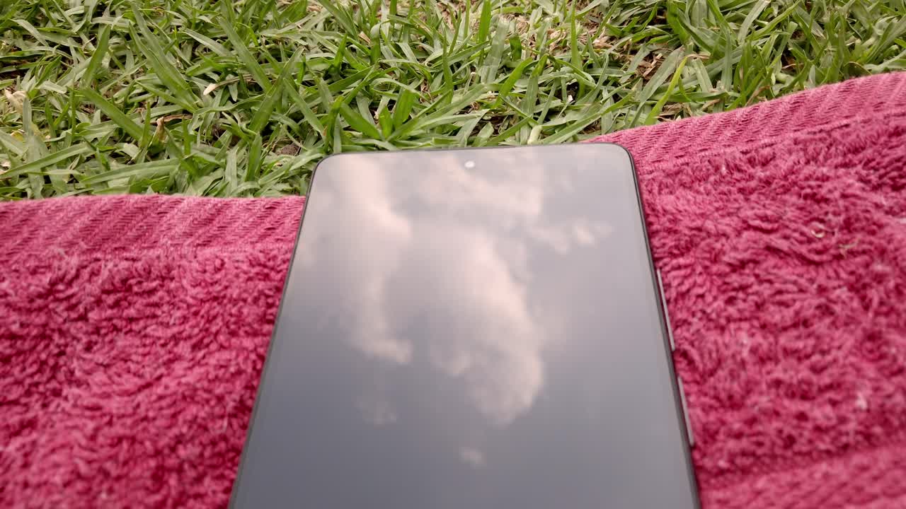 Push in shot of green grass with a red towel and mobile phones on it during the day in a garden, outdoor, close up