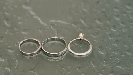 anillos de boda recién casados y anillo de compromiso en una superficie de vidrio con gotas de agua