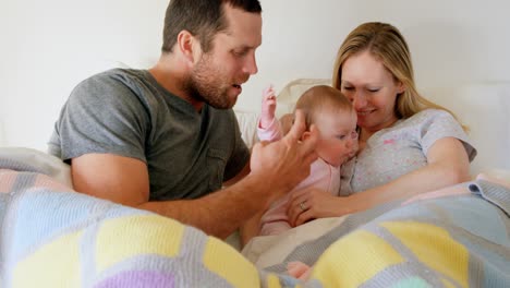 vista frontal de padres caucásicos adultos jugando con el bebé en la cama en un hogar cómodo 4k