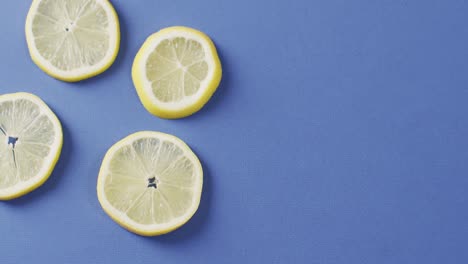 Video-of-slices-of-lemon-lying-on-blue-background-with-copy-space