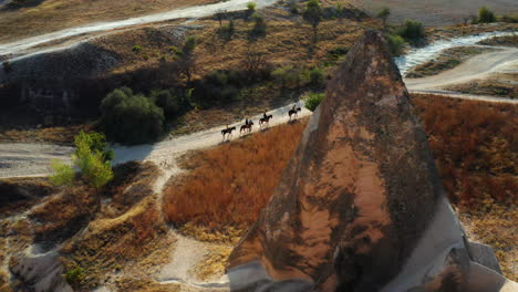 Flying-past-rock-formation-to-reveal-horse-riders-traveling-the-wild-of-Turkey-at-sunset