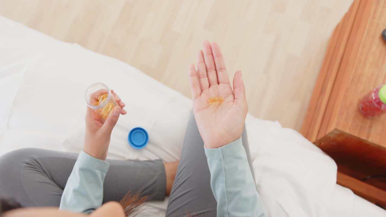 Holding pill bottle, asian woman pouring supplements into hand, at home
