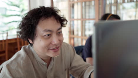 smiling asian man working by laptop in the cafe