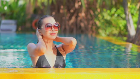 Sexy-sensual-woman-smooth-wet-hair-with-hands-while-standing-inside-private-swimming-pool-in-Bali,-Indonesia,-slow-motion-portrait