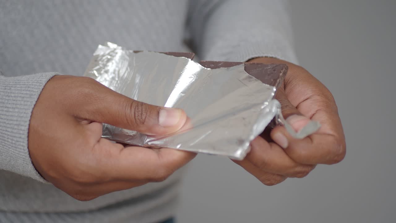 persona desempaquetando y comiendo chocolate oscuro