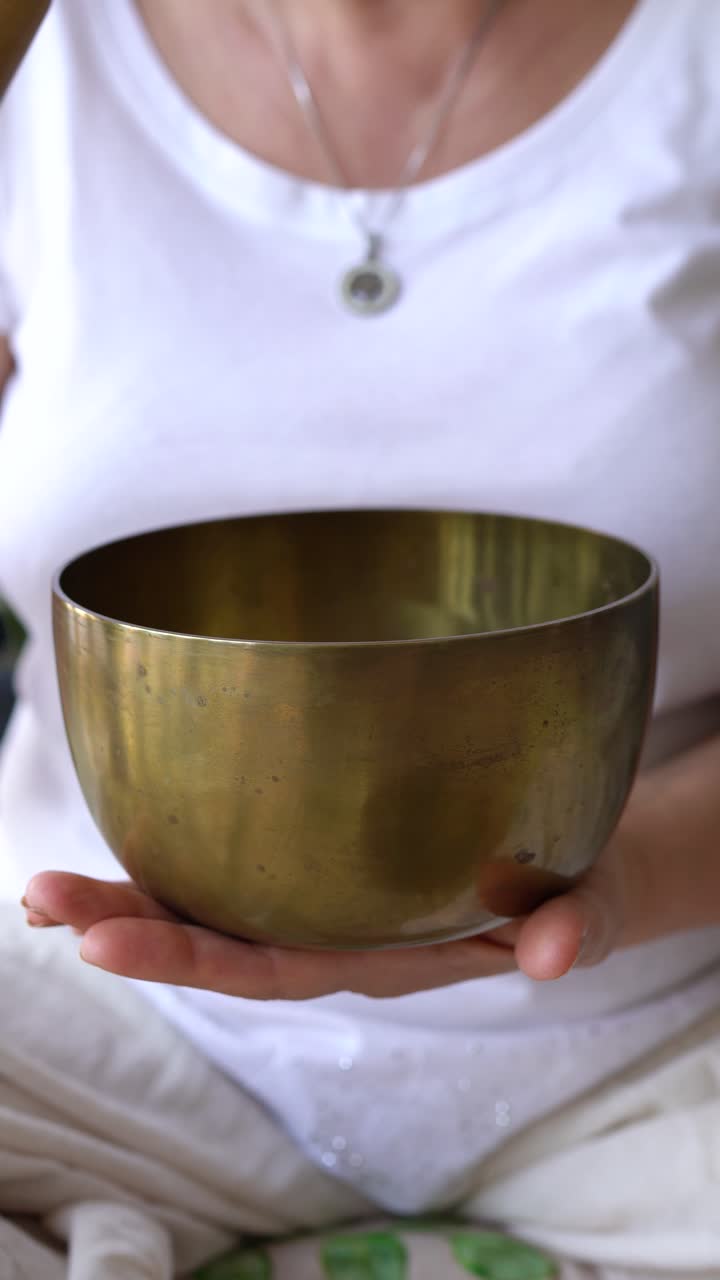 Woman Gently Rubs Suede-covered Mallet Around Tibetan Singing Bowl And Strikes It. closeup, vertical shot