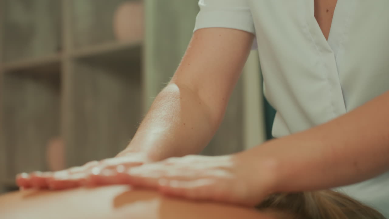 Estetista caucasica prepara olio e gel per un delicato massaggio alla schiena con microcorrente, mani che spalmano l'olio sulla schiena del cliente, illuminazione calda, stanza spa calma, terapista che usa movimenti lenti, clinico.