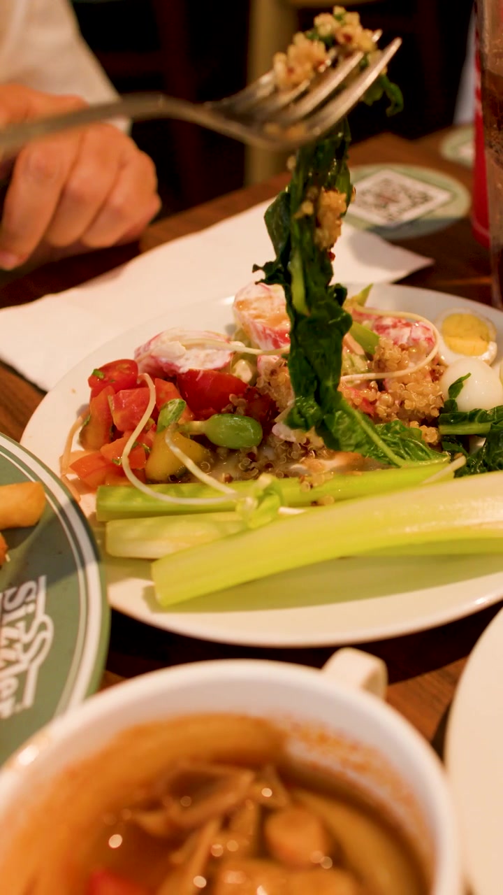 A person uses a fork to eat salad and vegetables at a restaurant table