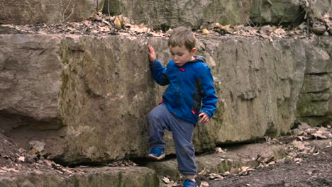 young boy exploring and climbing on a rock wall in the forest