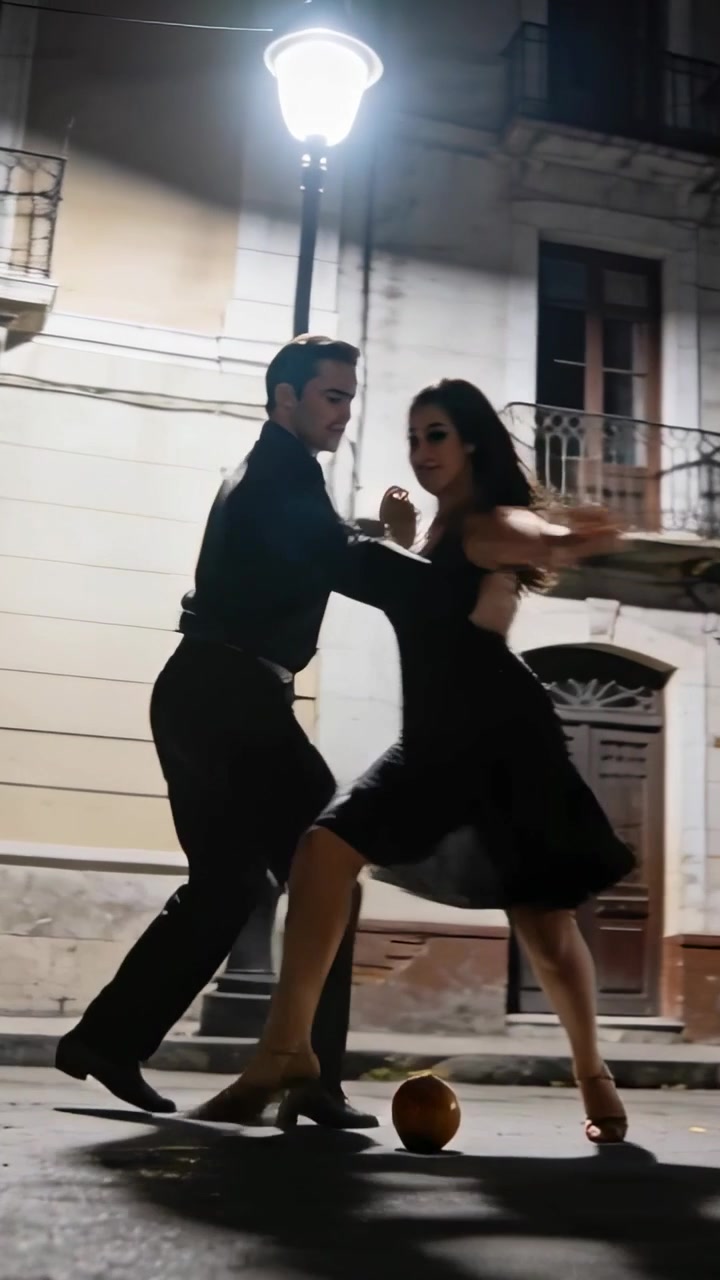 Video verticale: Lampada che illumina ballerini in nero che eseguono il tango come routine di strada con una palla arancione.