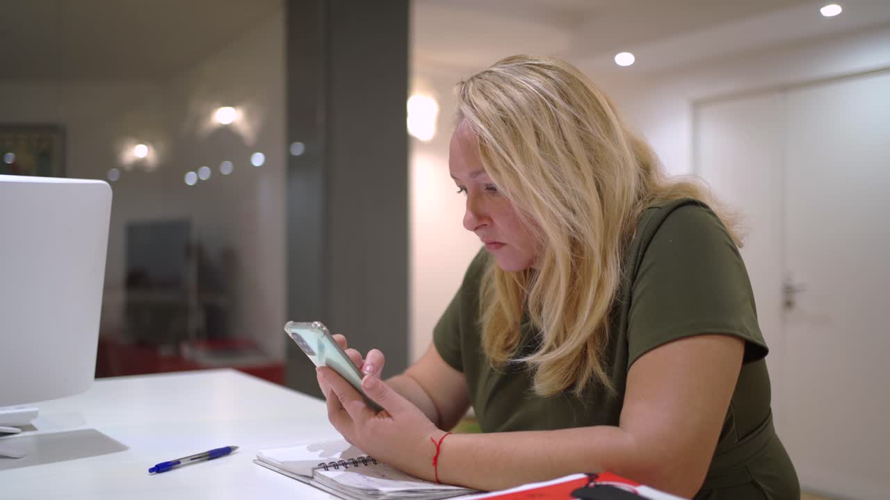 Woman browsing smartphone at table with notebook