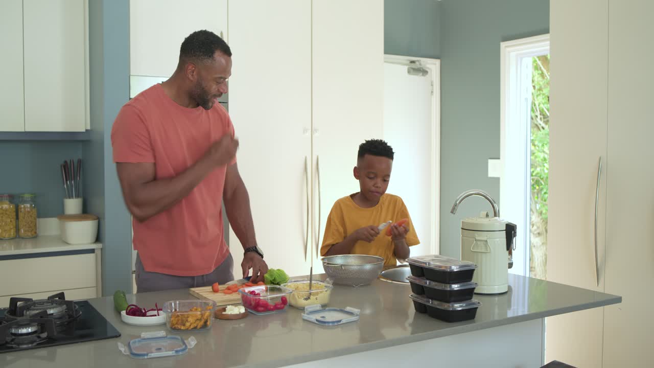 Padre e figlio in cucina: osservano contenitori impilati, tagliano carote su un tagliere e le sbucciano per pranzo.