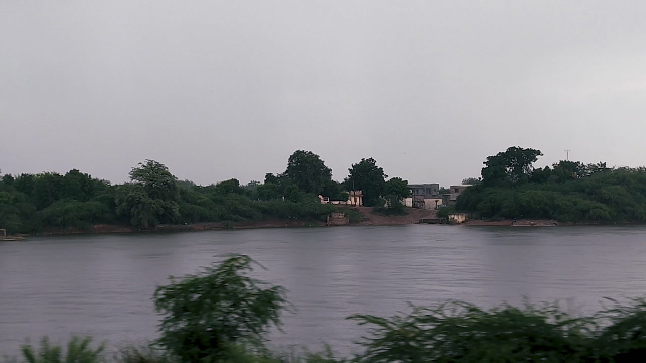 Serene shot from moving train. lush greenery and river in landscape. Peaceful scene from India, beauty of rural life as train passes by.