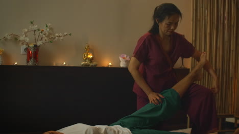 Asian-Woman-performs-Traditional-Thai-Massage-to-beautiful-European-Woman.-Rehabilitation-and-Treatment-after-Injuries-with-the-help-of-Massage.-Relax-and-Rest-from-massage-of-Legs-Arms-and-Back.-Therapeutic-massage