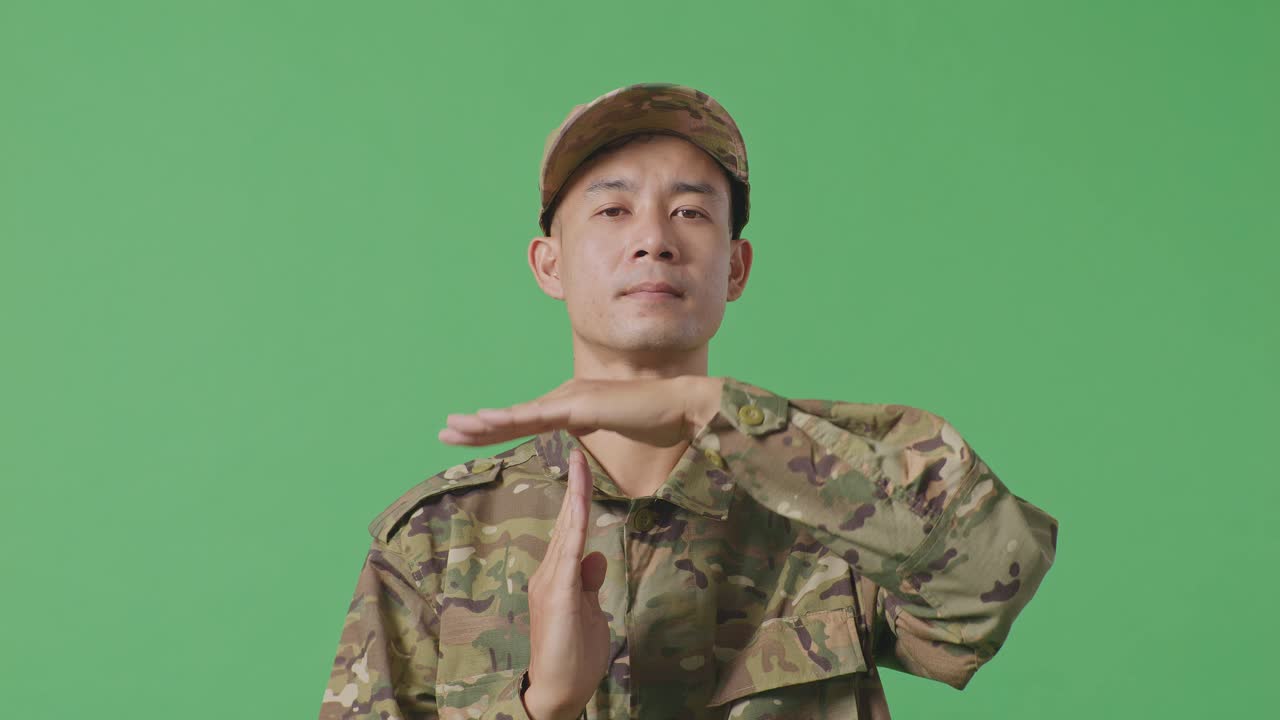 Close Up Of Asian Man Soldier Looking At Camera And Showing Time Out Hands Gesture While Standing In The Green Screen Background Studio