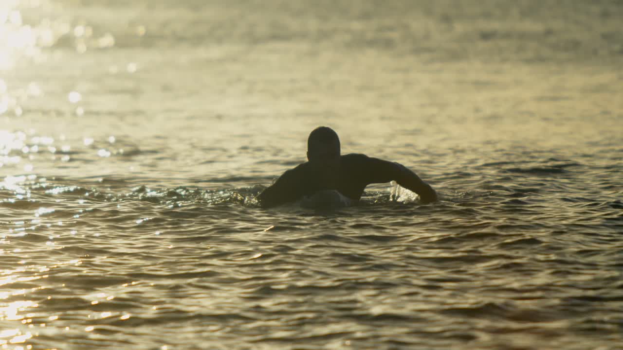 vista frontal de un surfista masculino nadando sobre una tabla de surf en el mar durante la puesta de sol 4k