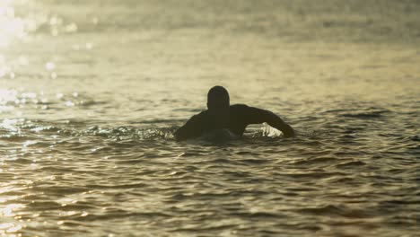 front view of male surfer swimming over surfboard in sea during sunset 4k