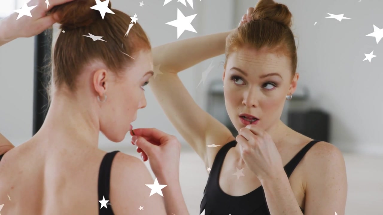Vertical video: Prepping dancer in black leotard smoothing bun, applying balm at mirror with stars