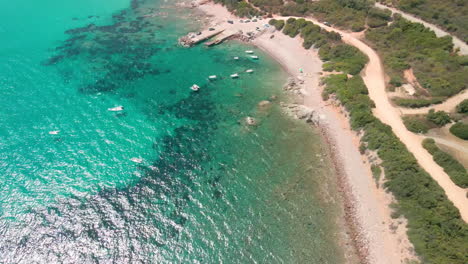 Vista-Panorámica-De-La-Hermosa-Costa-Mediterránea-Con-Mar-Azul-Tropical-Y-Barcos-Amarrados-Bajo-El-Sol-De-Verano-En-Cerdeña,-Italia---Toma-Aérea-De-Drones