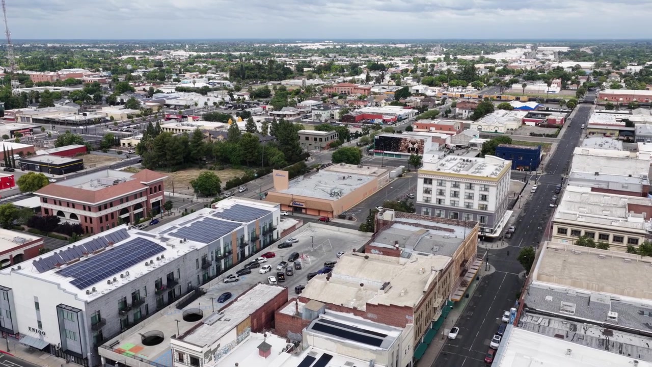 Tetti con pannelli solari coronano densi edifici storici del centro di Stockton, auto parcheggiate fiancheggiano strade a griglia che si estendono verso la vasta città della Central Valley molto più in basso. Sorvolo aereo con drone
