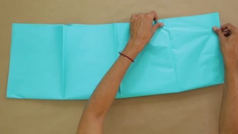 folding large blue tissue paper on table with hands, viewed from above in close-up shot