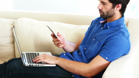 Hombre-Sentado-En-Un-Sofá-Usando-Su-Computadora-Portátil-Y-Llamando-Por-Teléfono