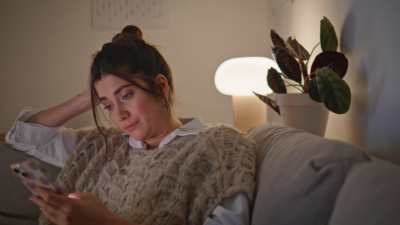 근접 촬영 피곤한 소녀가 드폰을 탐색하고 램프 빛에 어두운 방에서 문자를 읽고 있습니다.