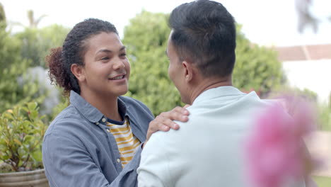 feliz pareja de hombres homosexuales diversos hablando y sonriendo sentados en un jardín soleado, cámara lenta