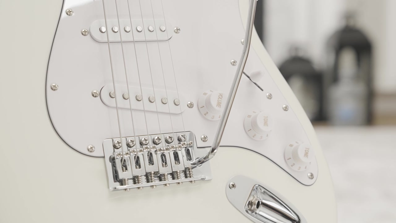 Nærbillede af en hvid elguitar i Stratocaster-stil i en stue.