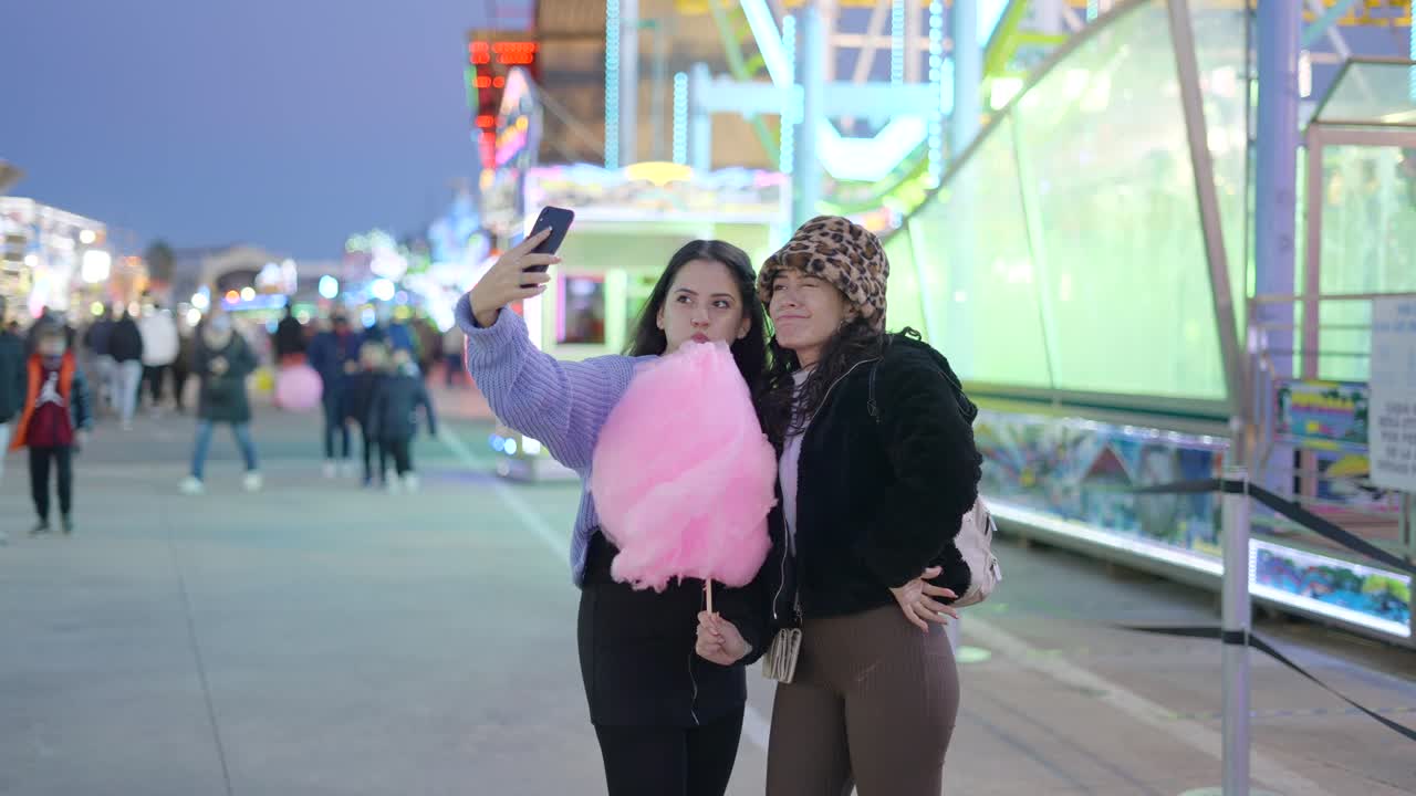 Two Friends Taking a Selfie at a Night Fair with Cotton Candy