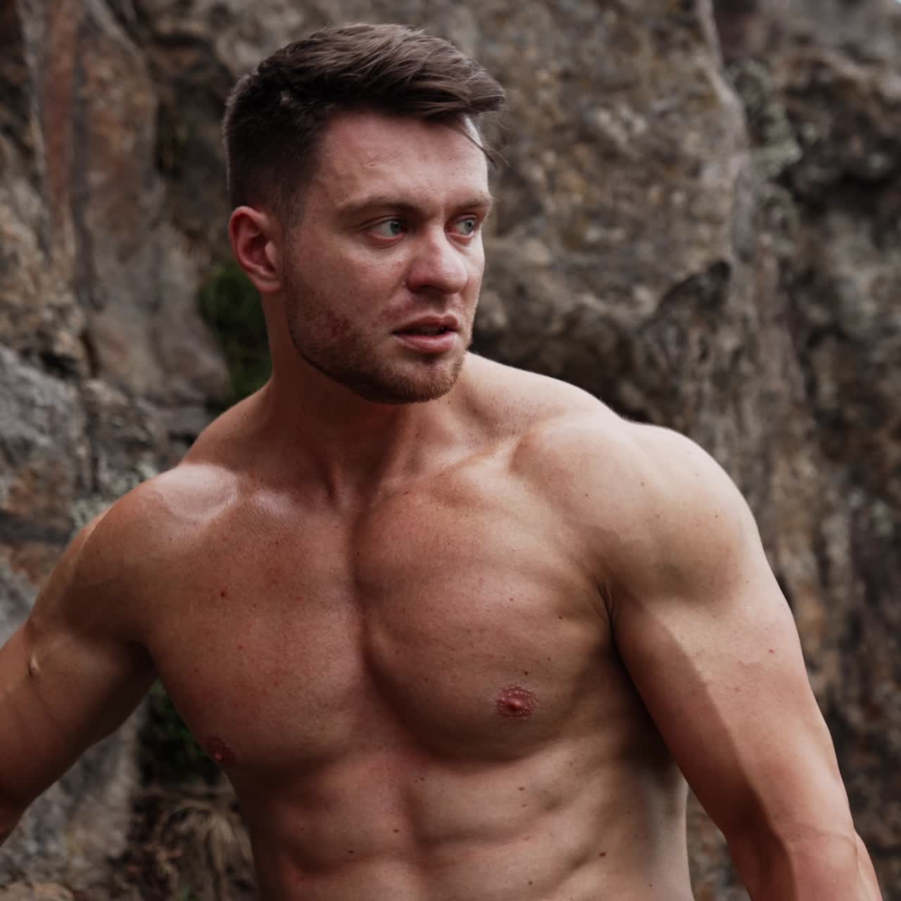 Handsome muscular Caucasian man stands at the rock. Sportsman with naked torso working out in the nature