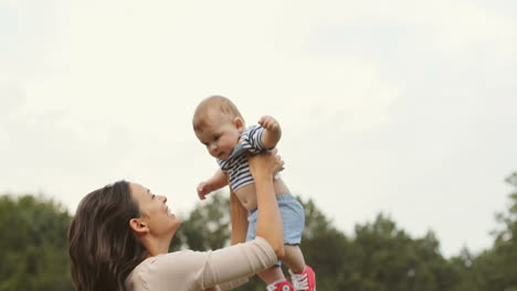 happy mother tossing up her cute toddler son in the park