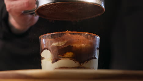 sifting cocoa powder over tiramisu dessert. - closeup shot