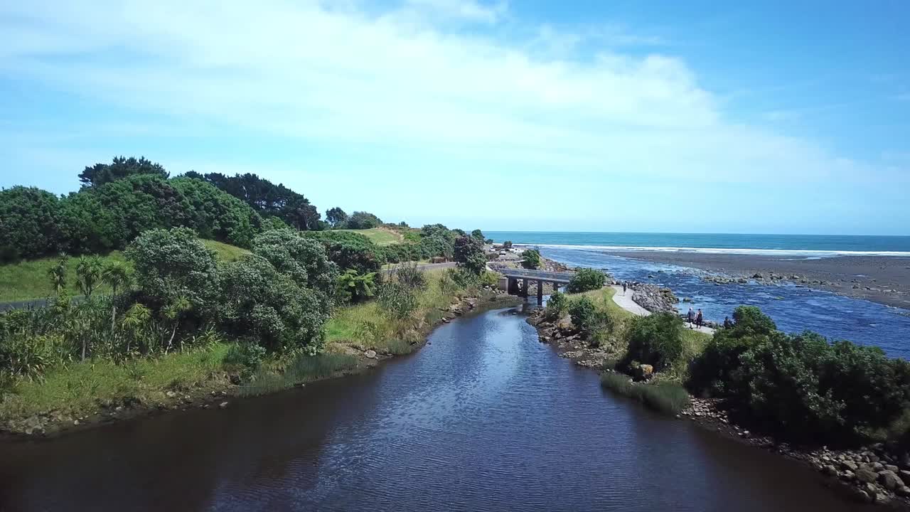 Aerial drone shot, flying over lake towards a bridge into the ocean on a sunny day in New Plymouth, New Zealand