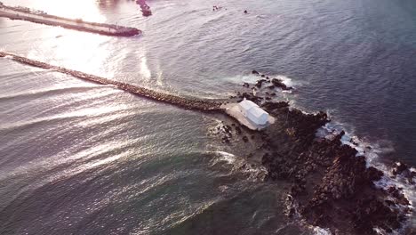 Romantic-white-chapel-in-Mediterranean-sea-during-sunset,-aerial-orbit-view