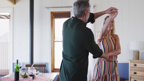 feliz pareja caucásica madura bailando en la sala de estar soleada