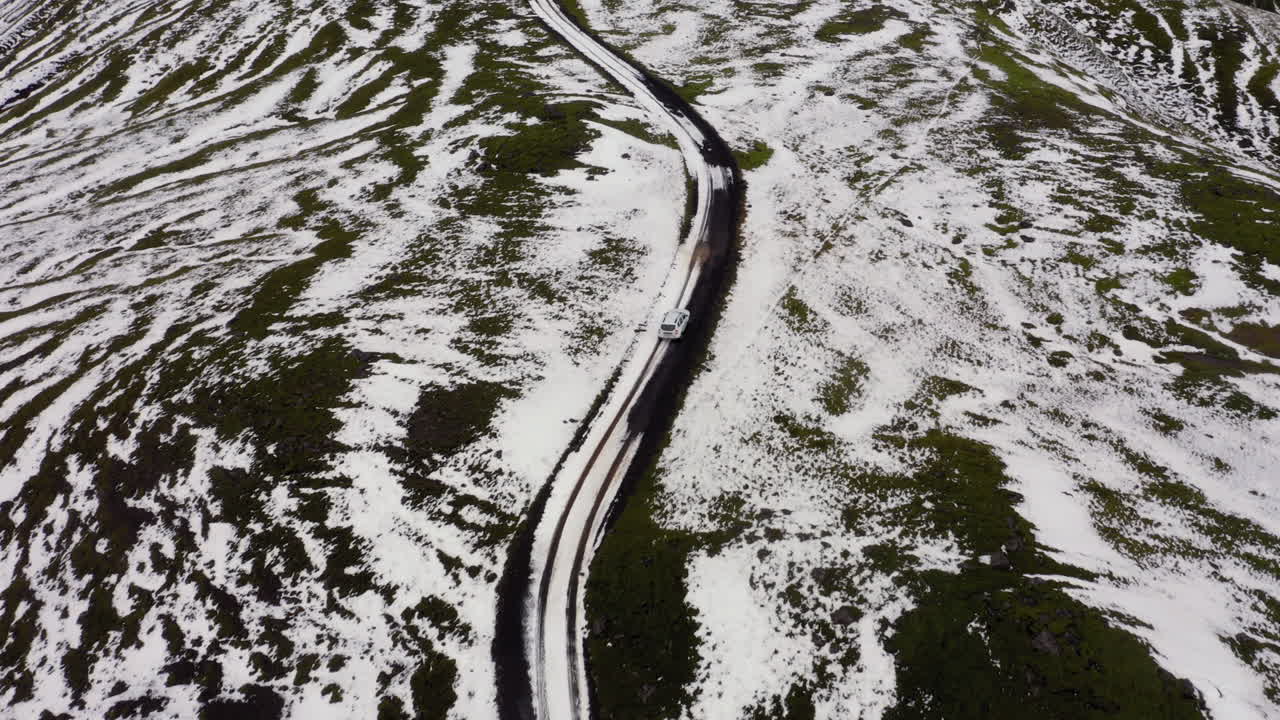 Aerial: Following a white car on muddy dirt road, partially covered with snow