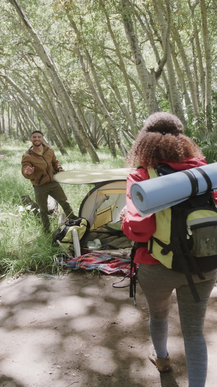 Vertical video of biracial couple pitching tent in forest, slow motion
