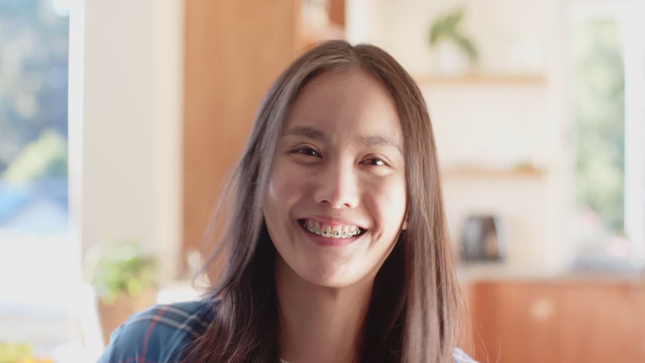 Smiling asian teenage girl with braces looking at camera in bright indoor setting, copy space