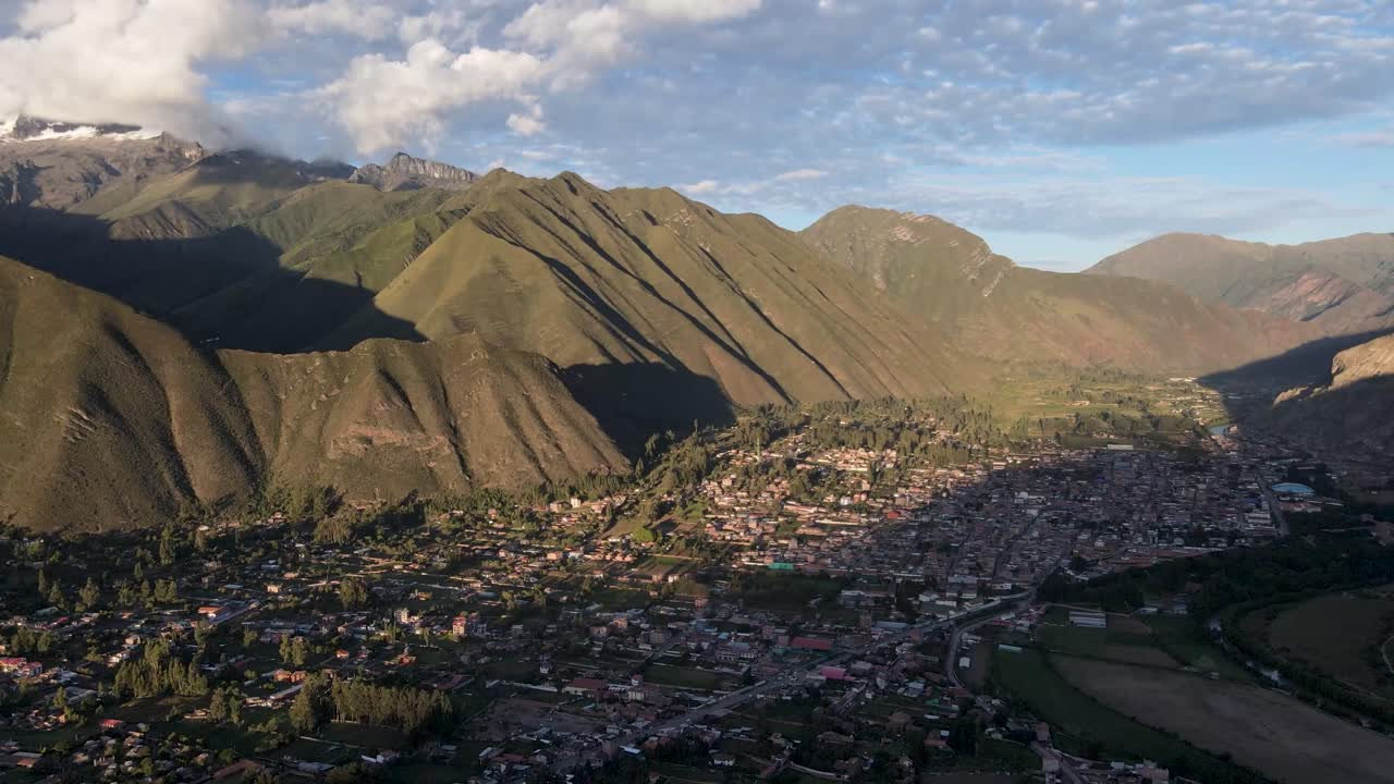 Ripresa con drone della Valle Sacra con un villaggio e una gigantesca catena montuosa illuminata dal sole a Cusco, Perù.